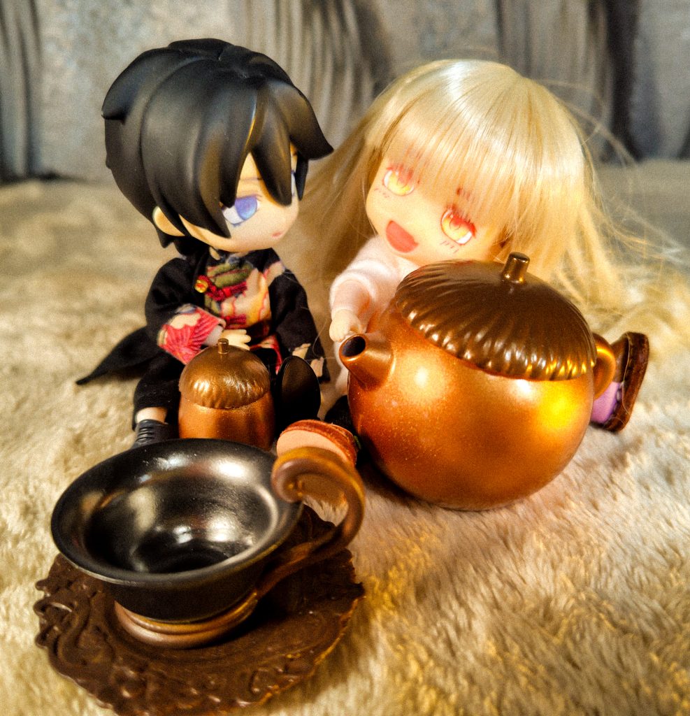 おおきなどんぐり型のティーポッドを持った小さなドールがもう一人のドールに笑いかけている