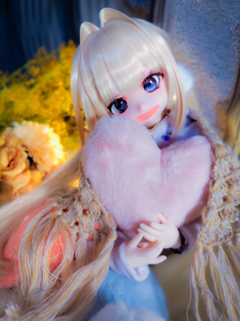 ハートのクッションを抱きかかえた少女のドールが笑っている