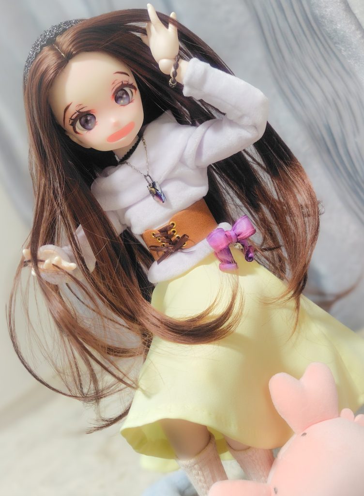 長い茶髪を風になびかせた少女のドールが微笑んでいる
