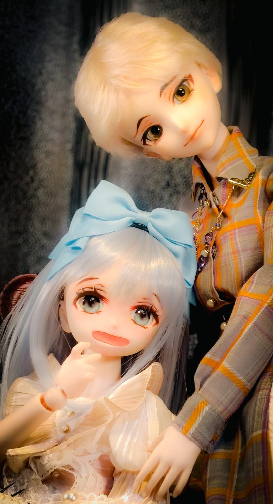 身長の高いドールが少女のドールに身寄せてたたずんでいる