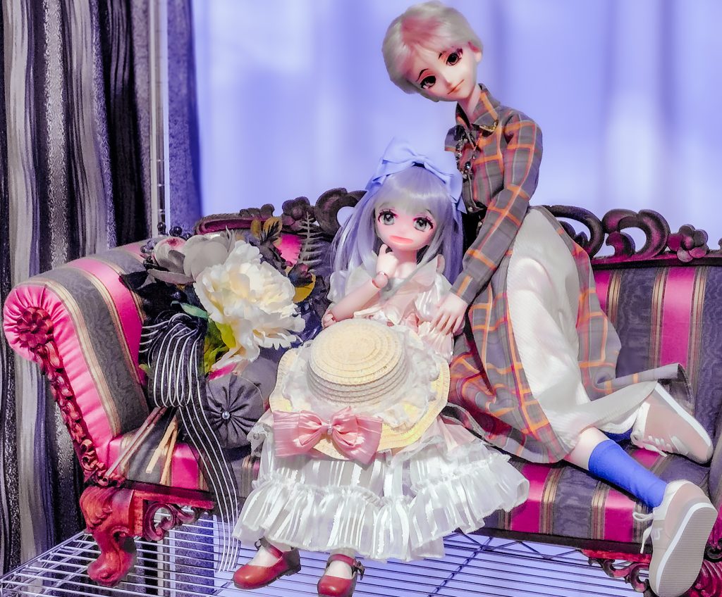 中世的なソファの上に膝立ちした女性ドールが少女ドールに寄り添っている